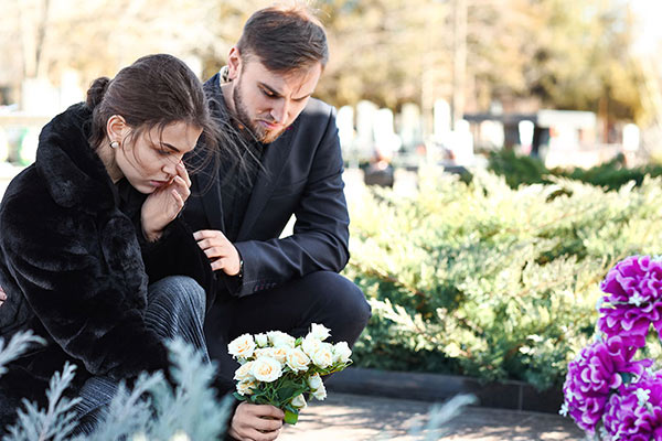 2 people placing flowers by a grave